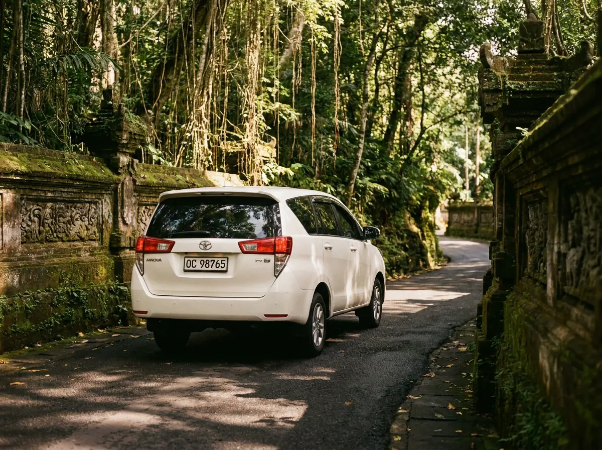 Pearl-white Toyota Innova driving a jungle road between carved Balinese stone walls